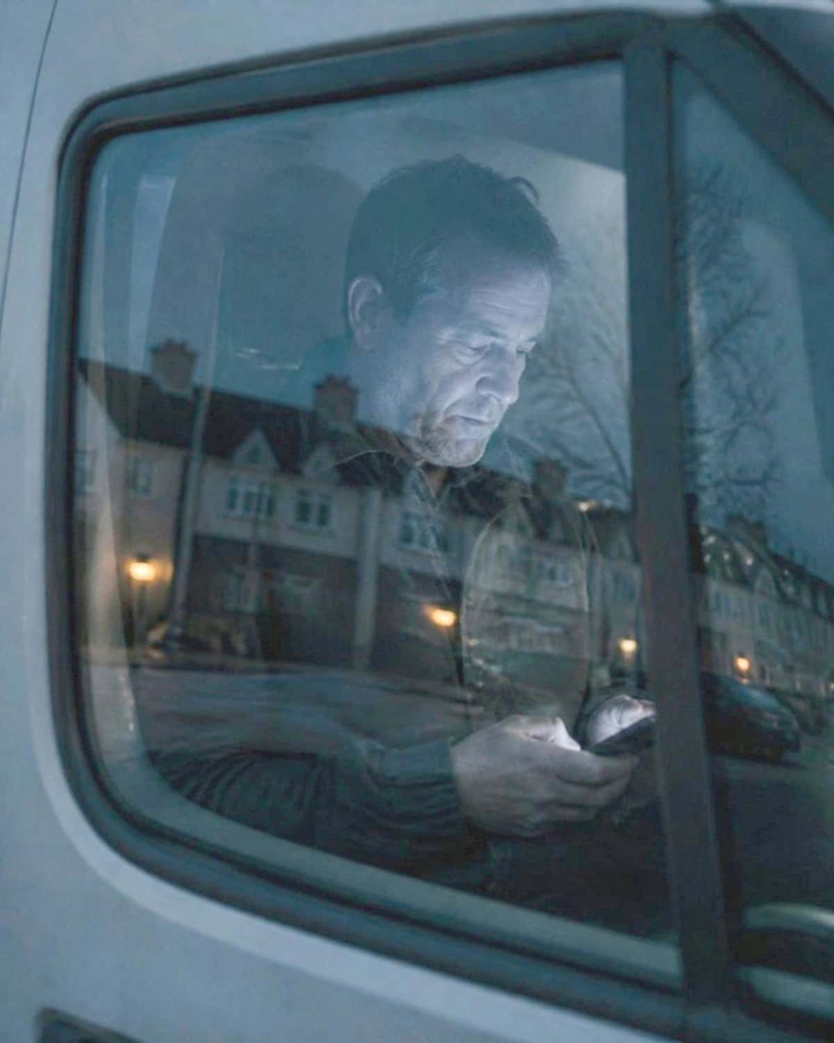 A firm's owner in the cab of his van at dusk, reading his phone