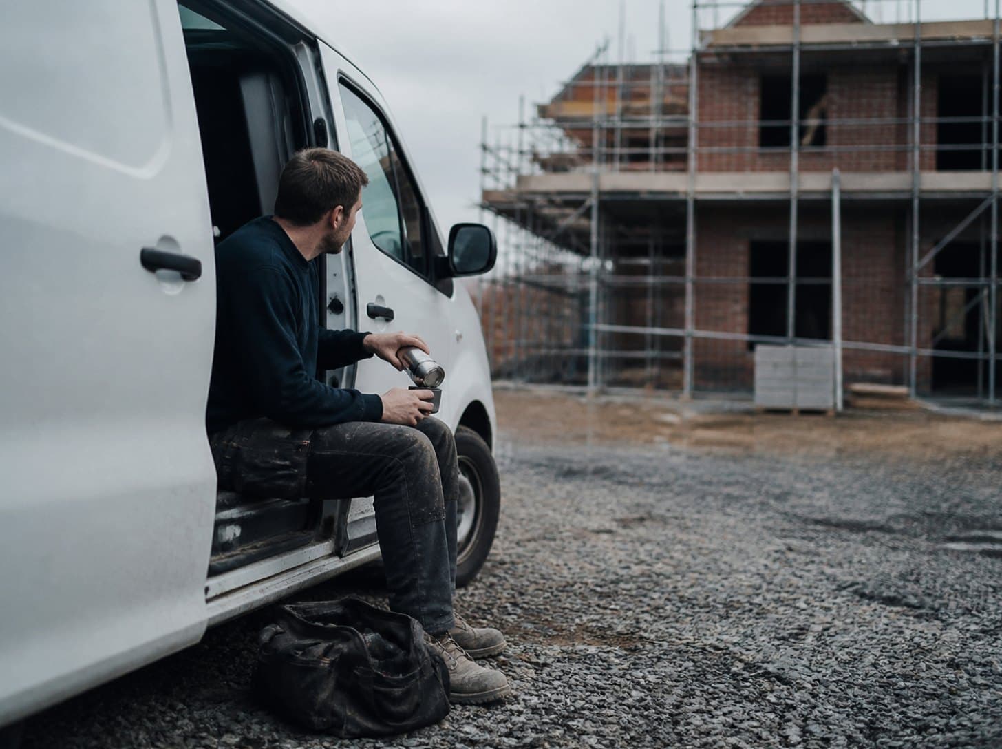 A tradesman pouring tea from a flask on the step of his van at lunch